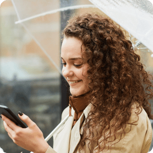 Woman with brown curly hair looking at cell phone holding umbrella