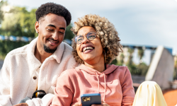 smiling man and woman outside looking at a phone